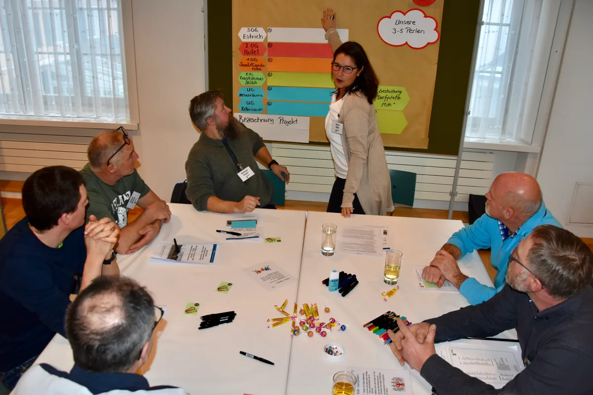 Eine Frau zeigt auf eine Pinnwand, wo mehrere farbige Zettel hängen. 